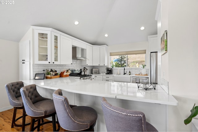 kitchen featuring a sink, vaulted ceiling, stainless steel appliances, and wall chimney exhaust hood