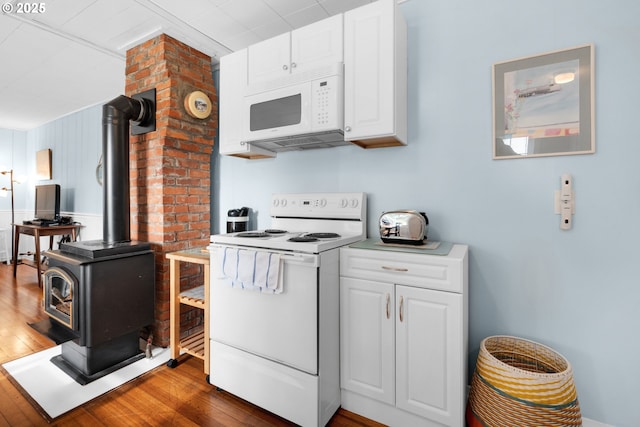 kitchen with white appliances, white cabinets, dark wood finished floors, and a wood stove