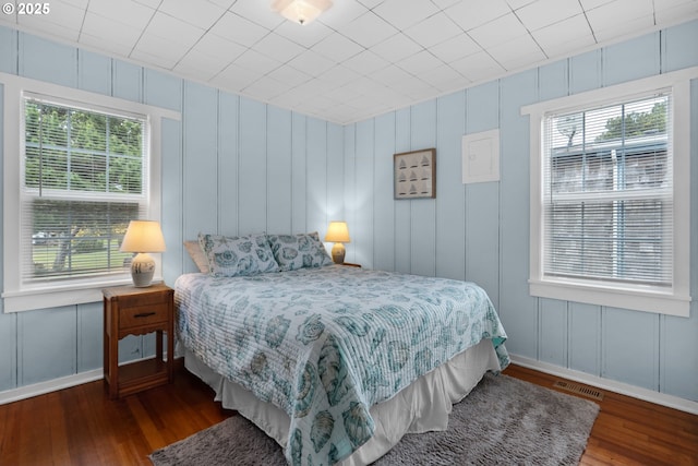 bedroom with visible vents, a decorative wall, baseboards, and wood finished floors