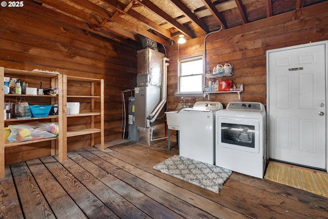 clothes washing area featuring wooden walls, a sink, water heater, independent washer and dryer, and hardwood / wood-style floors