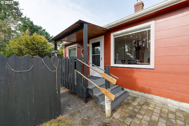 view of side of home featuring entry steps, a gate, a chimney, and fence