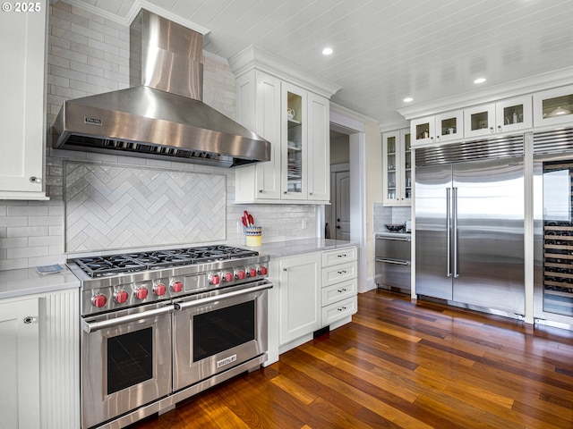 kitchen featuring high quality appliances, wall chimney exhaust hood, light countertops, crown molding, and tasteful backsplash