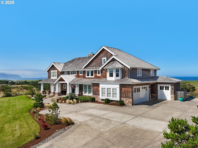 shingle-style home with concrete driveway, a chimney, stone siding, a front lawn, and a porch