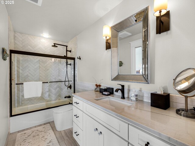 bathroom with combined bath / shower with glass door, toilet, and vanity
