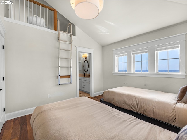 bedroom featuring wood finished floors, vaulted ceiling, baseboards, and ensuite bath