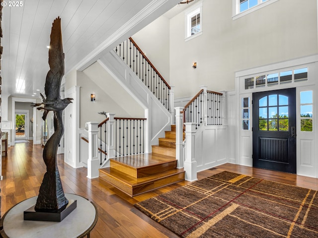 entryway with hardwood / wood-style floors, stairs, a towering ceiling, crown molding, and a decorative wall