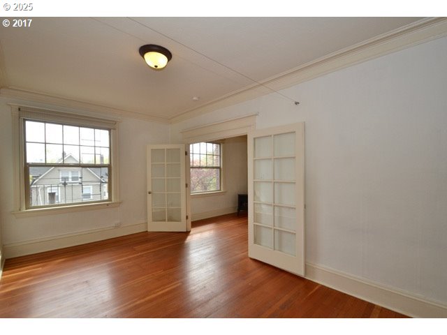 empty room featuring french doors, ornamental molding, wood finished floors, and baseboards