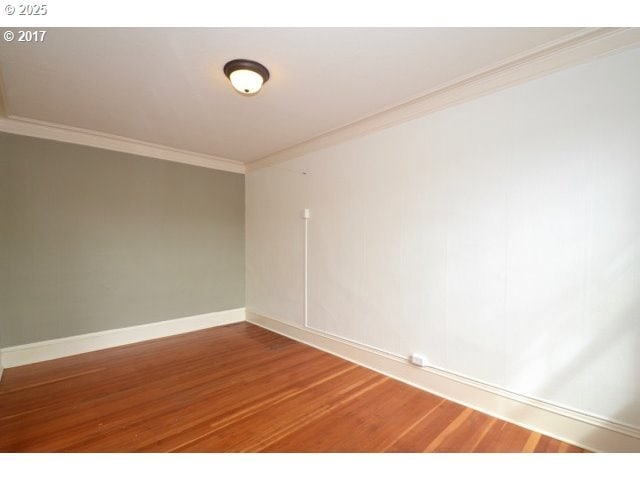 empty room featuring baseboards, wood finished floors, and crown molding