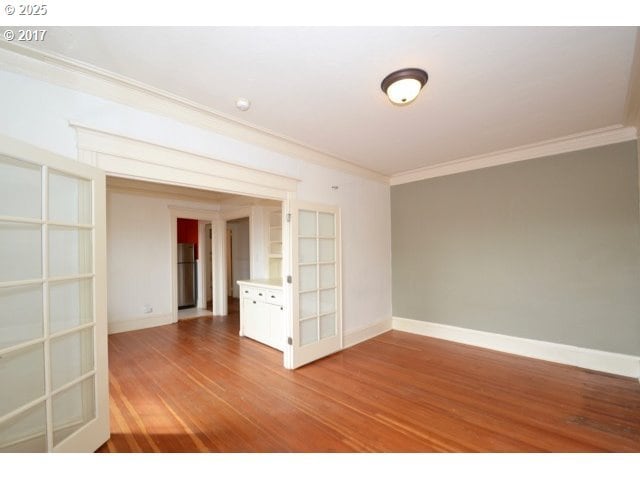 spare room featuring ornamental molding, baseboards, and wood finished floors