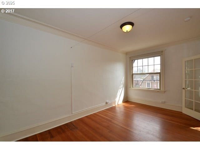 spare room with ornamental molding, wood finished floors, and baseboards