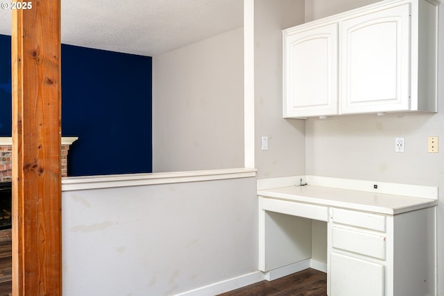 unfurnished office featuring baseboards, a textured ceiling, dark wood-style flooring, and built in desk
