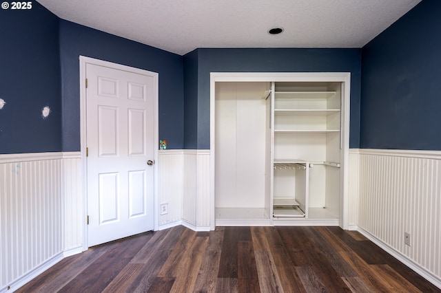 unfurnished bedroom featuring a closet, a textured ceiling, a wainscoted wall, and wood finished floors