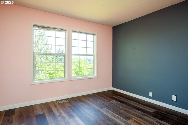 spare room featuring baseboards, visible vents, and dark wood-type flooring