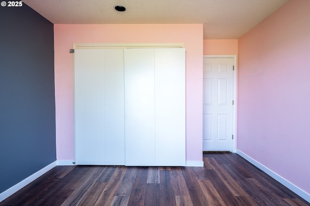 unfurnished bedroom with baseboards, a closet, and dark wood-style flooring