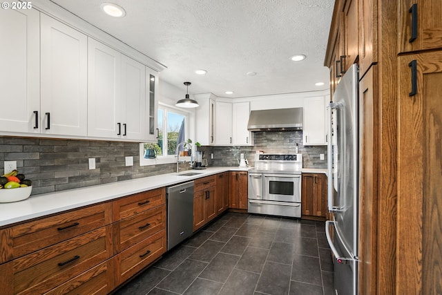 kitchen featuring stainless steel appliances, light countertops, a sink, and wall chimney exhaust hood