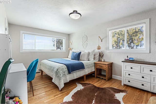 bedroom featuring light wood-style floors, multiple windows, a textured ceiling, and a textured wall