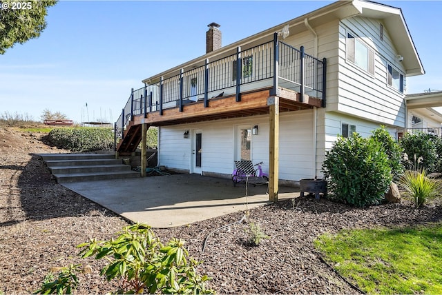 back of house with stairs, a chimney, a patio area, and a wooden deck