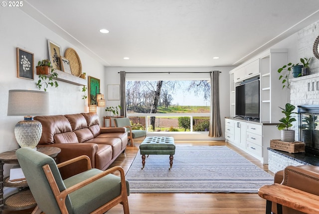 living area featuring light wood finished floors, a glass covered fireplace, and recessed lighting