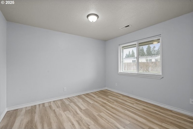 empty room featuring visible vents, baseboards, a textured ceiling, and light wood-style flooring