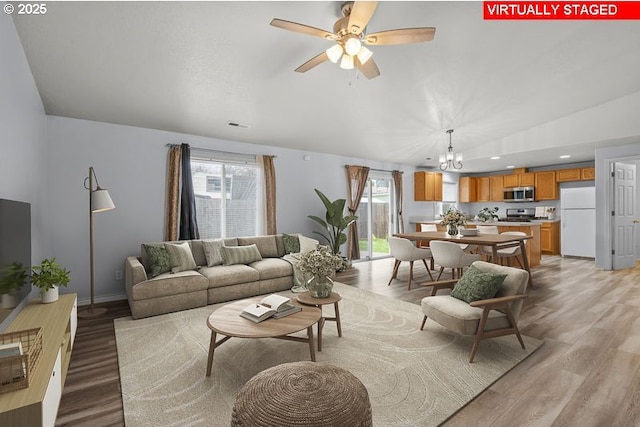 living area featuring vaulted ceiling, ceiling fan with notable chandelier, light wood-type flooring, and visible vents