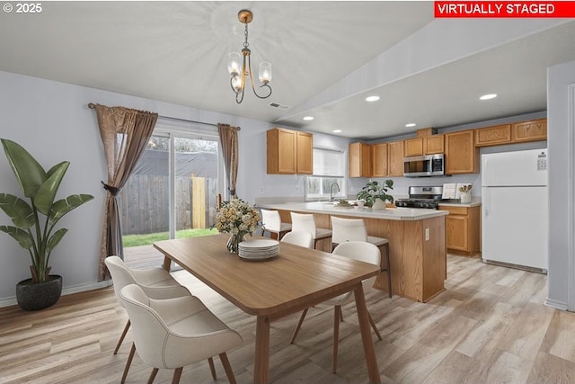 dining space featuring vaulted ceiling, a notable chandelier, light wood-style floors, and a wealth of natural light