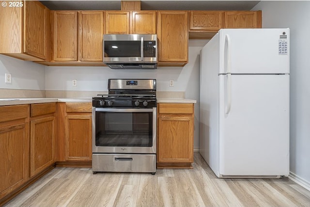 kitchen with brown cabinets, light wood-style floors, appliances with stainless steel finishes, and light countertops