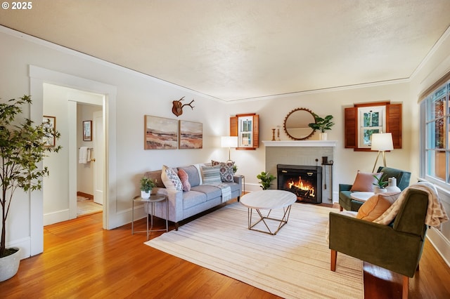 living area featuring a brick fireplace, crown molding, baseboards, and light wood-style flooring