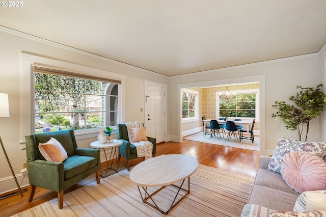 living room with crown molding, baseboards, an inviting chandelier, and light wood finished floors
