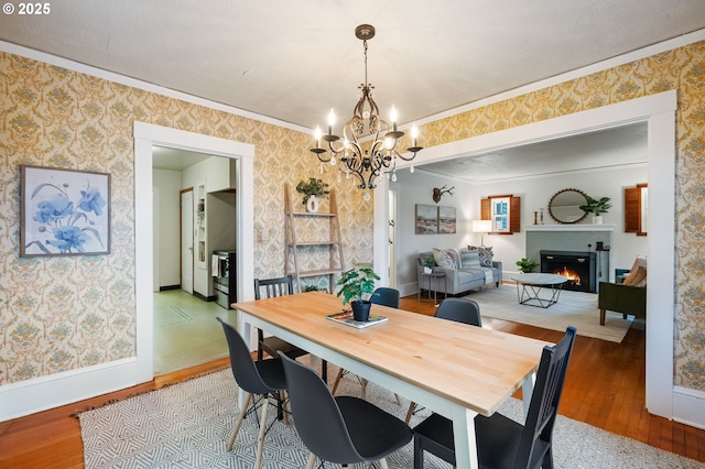 dining room featuring crown molding, wallpapered walls, a chandelier, and wood finished floors