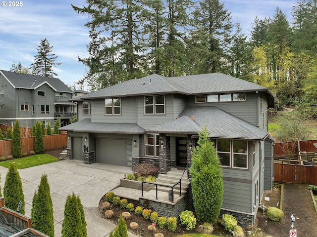 prairie-style home with concrete driveway, stone siding, a garage, fence, and a shingled roof