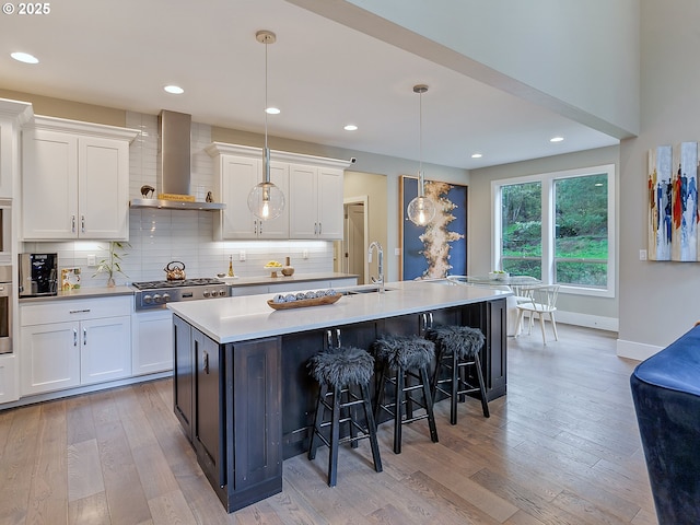 kitchen with wall chimney range hood, light wood finished floors, white cabinetry, and appliances with stainless steel finishes