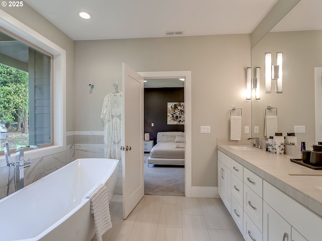 bathroom with a freestanding tub, double vanity, tile patterned floors, visible vents, and a sink
