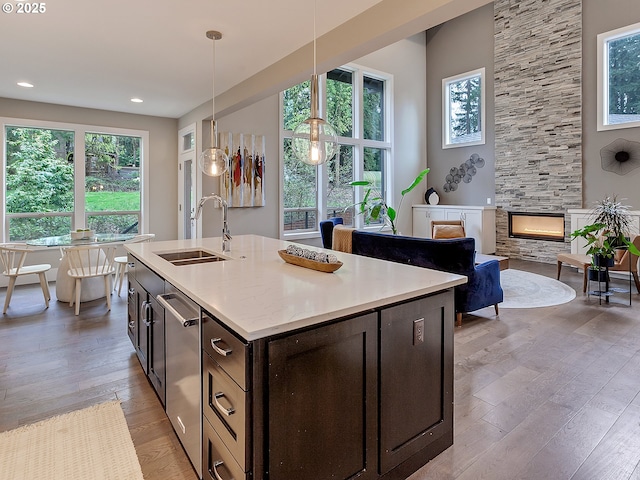 kitchen with a wealth of natural light, dark brown cabinetry, a stone fireplace, a sink, and light wood finished floors