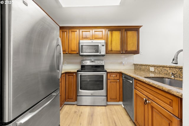 5130 SW Multnomah Blvd Unit H, Portland, OR 97219 - kitchen featuring stainless steel appliances, brown cabinets, light wood-style floors, tasteful backsplash, and light stone countertops