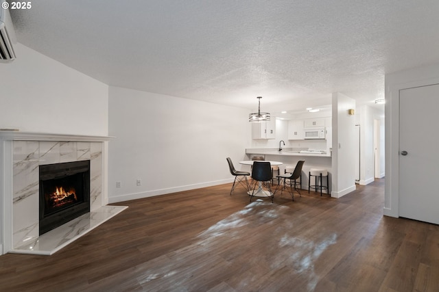 living area featuring a textured ceiling, dark wood-type flooring, a wall mounted AC, a premium fireplace, and baseboards