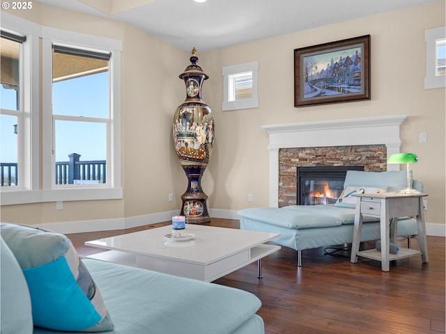 living room with dark wood-style flooring, a stone fireplace, and baseboards