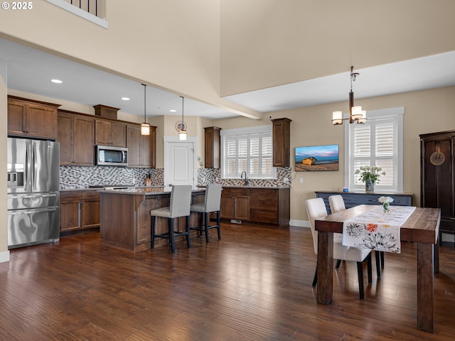 interior space with stainless steel appliances, dark wood-type flooring, a kitchen island, a kitchen breakfast bar, and backsplash