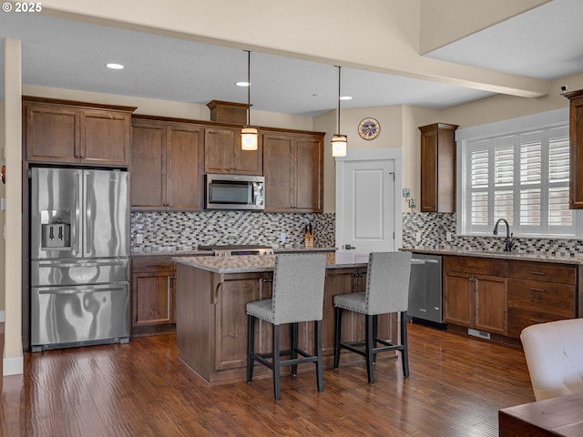 kitchen featuring light stone counters, stainless steel appliances, dark wood-style flooring, a kitchen island, and backsplash