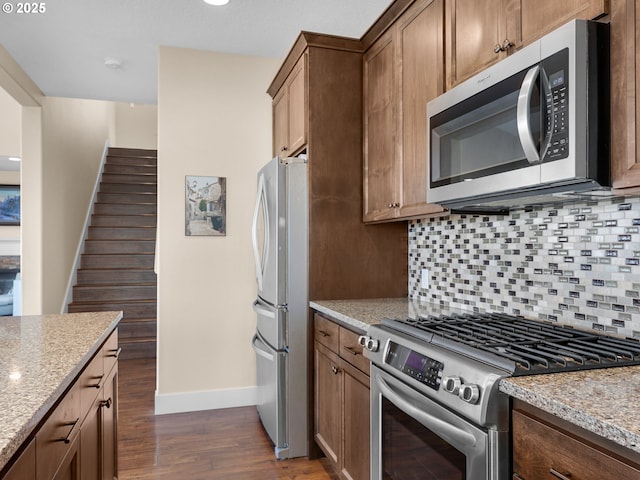 kitchen with backsplash, light stone counters, stainless steel appliances, and dark wood finished floors