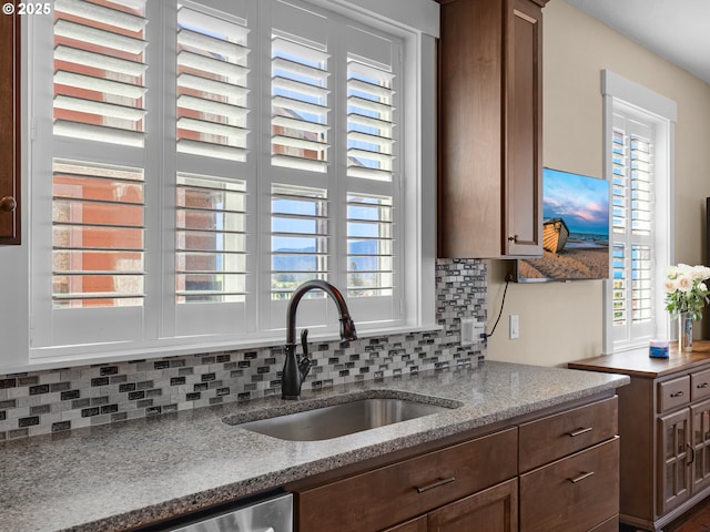 kitchen with stainless steel dishwasher, light stone counters, decorative backsplash, and a sink