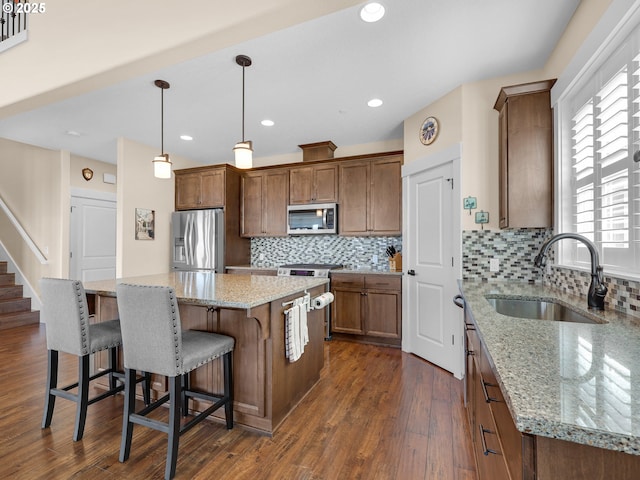 kitchen with dark wood-style floors, a center island, tasteful backsplash, appliances with stainless steel finishes, and a sink