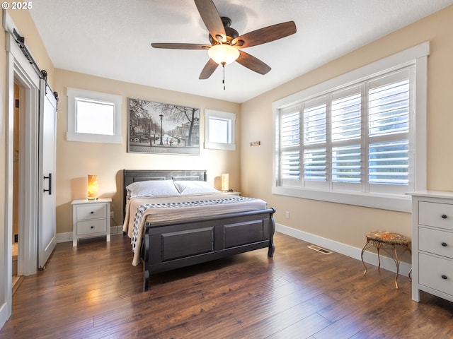 bedroom featuring dark wood-style floors, a barn door, visible vents, and baseboards