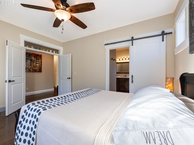 bedroom featuring a barn door, dark wood-type flooring, a ceiling fan, connected bathroom, and baseboards