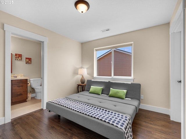 bedroom with ensuite bath, baseboards, visible vents, and wood finished floors