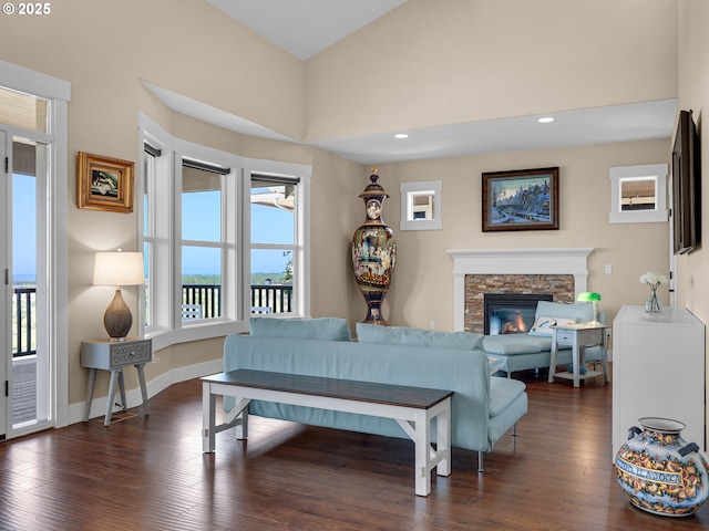 living room featuring dark wood-style floors, recessed lighting, a high ceiling, a stone fireplace, and baseboards