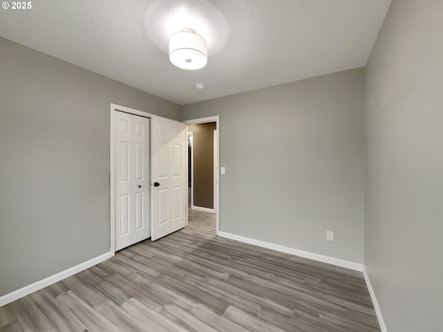 unfurnished bedroom featuring a textured ceiling, a closet, baseboards, and wood finished floors