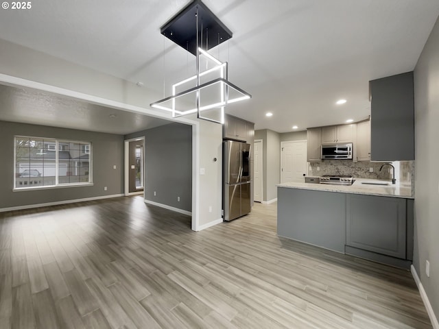 kitchen with open floor plan, stainless steel appliances, gray cabinetry, light wood-style floors, and backsplash