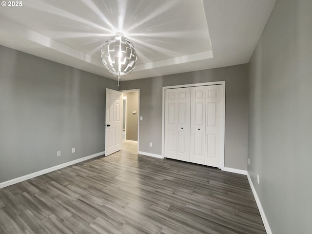 unfurnished bedroom with a tray ceiling, a closet, baseboards, and wood finished floors