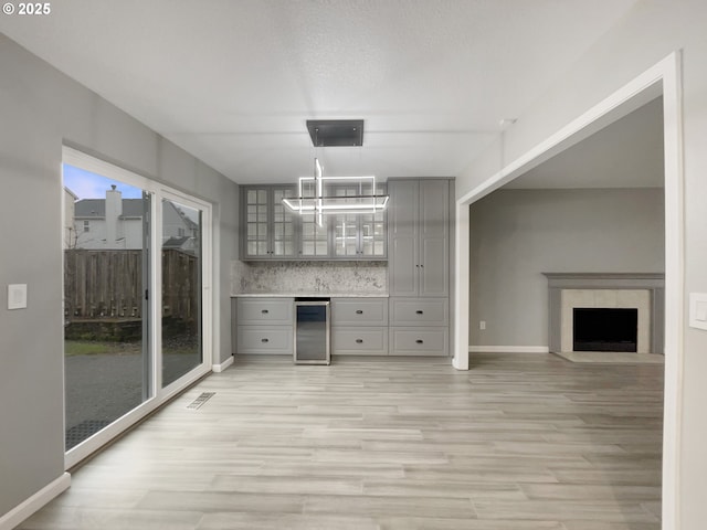 interior space featuring a fireplace, a dry bar, visible vents, light wood-style floors, and beverage cooler