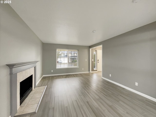 unfurnished living room featuring a tiled fireplace, wood finished floors, and baseboards